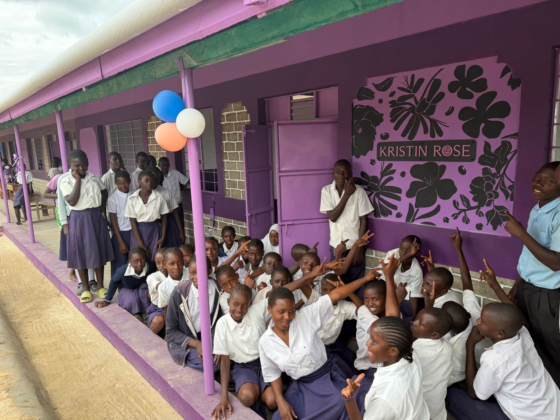 Students gathered outside their new classroom in Kenya, pointing to the Kristin Rose mural