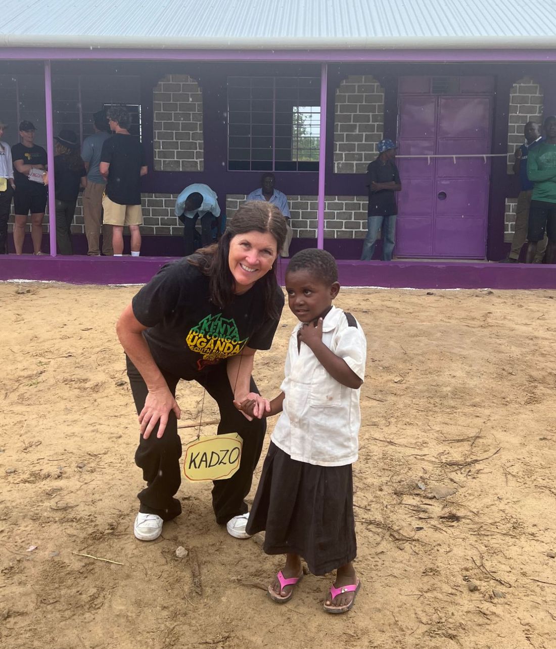 Kristin Rose smiling beside a young student in front of the new school in Kenya